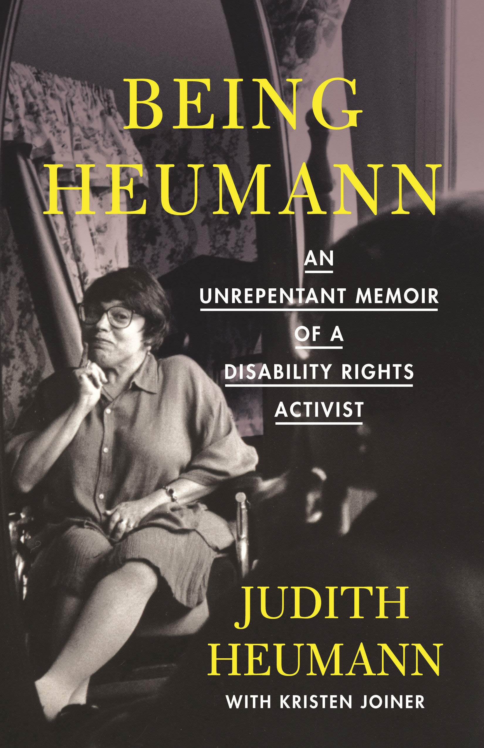 The cover of the hardcover version "Being Heumann by Judy Heumann and Kristen Joiner. A black and white picture of Judy with yellow tex reading "Being Heumann: An Unrepentant Memoir of a Disability Rights Activist"