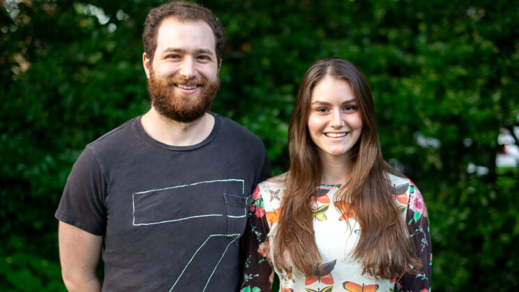 Image Description: A white man in a grey t-shirt with short dark hair and a beard smiling, a white woman with long dark hair, wearing a top with butterflies on it and smiling.