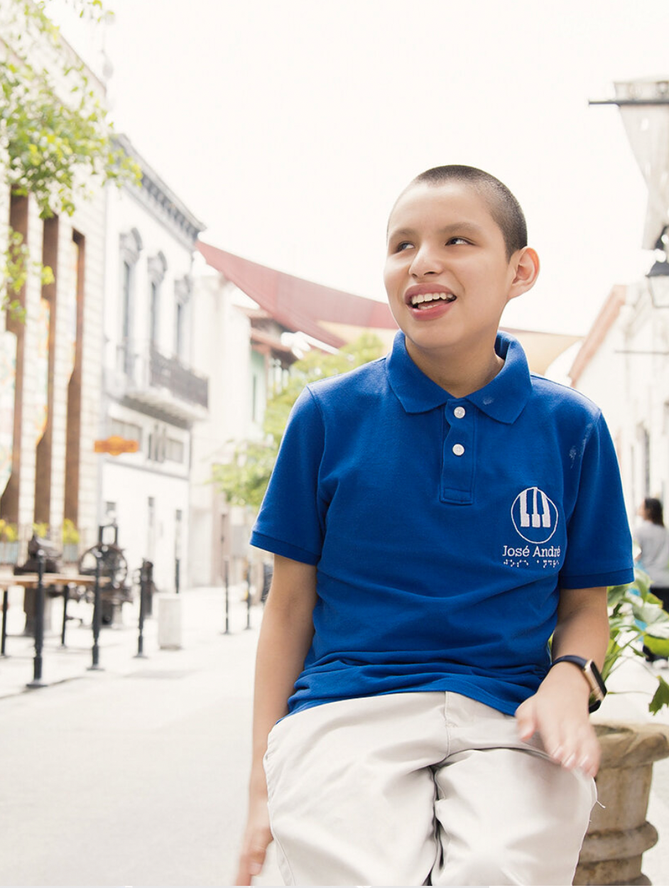 A photo of José André, a blind latino teenage boy with shaved brown hair wearing a blue polo shirt with his name embroidered in white and khaki pants.