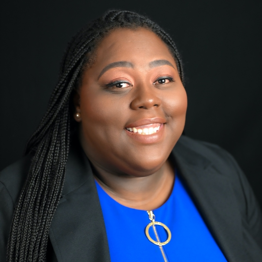 A headshot of YT Bell, a Black woman with long black braids wearing a blue top and black blazer.