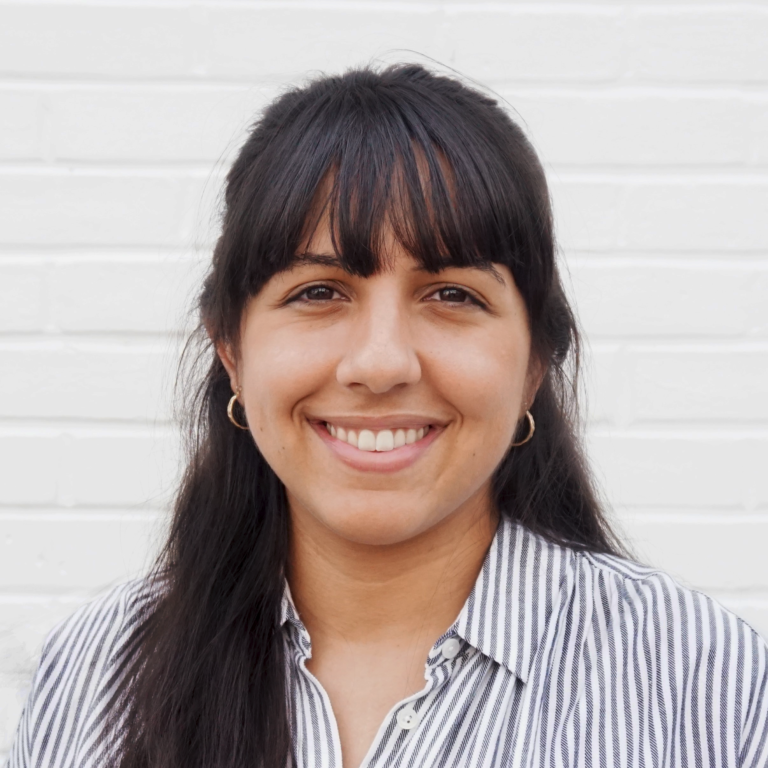 Headshot of Lilian Aluri, a woman with brown skin and long brown hair with bangs wearing hoop earrings and a white and blue striped shirt.