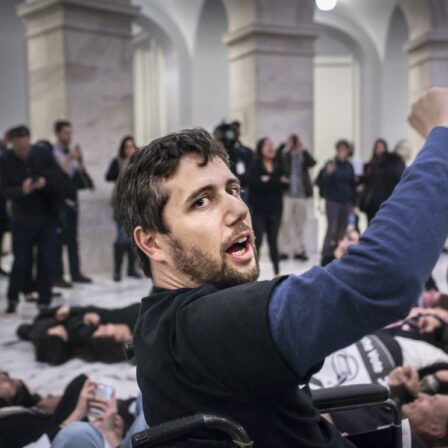 A photo of Ady Barkan in a manual wheelchair with his fist raised.