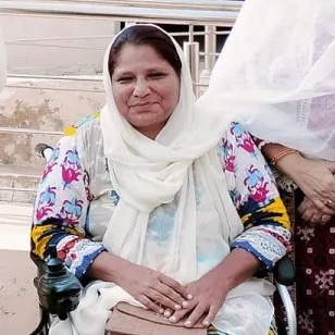 Photo of Zahina Hameed, a Pakistani woman who uses a motorized wheelchair wearing a white headscarf, and a colorful shirt.