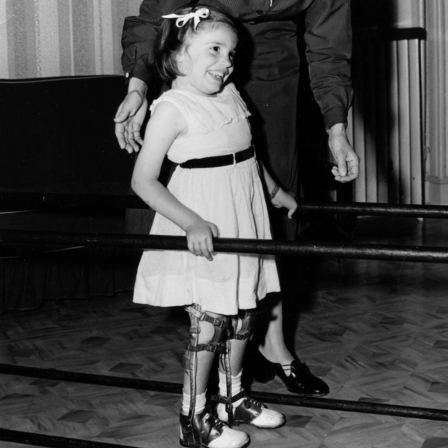 Judy as a child walking with braces on her legs holding two bars
