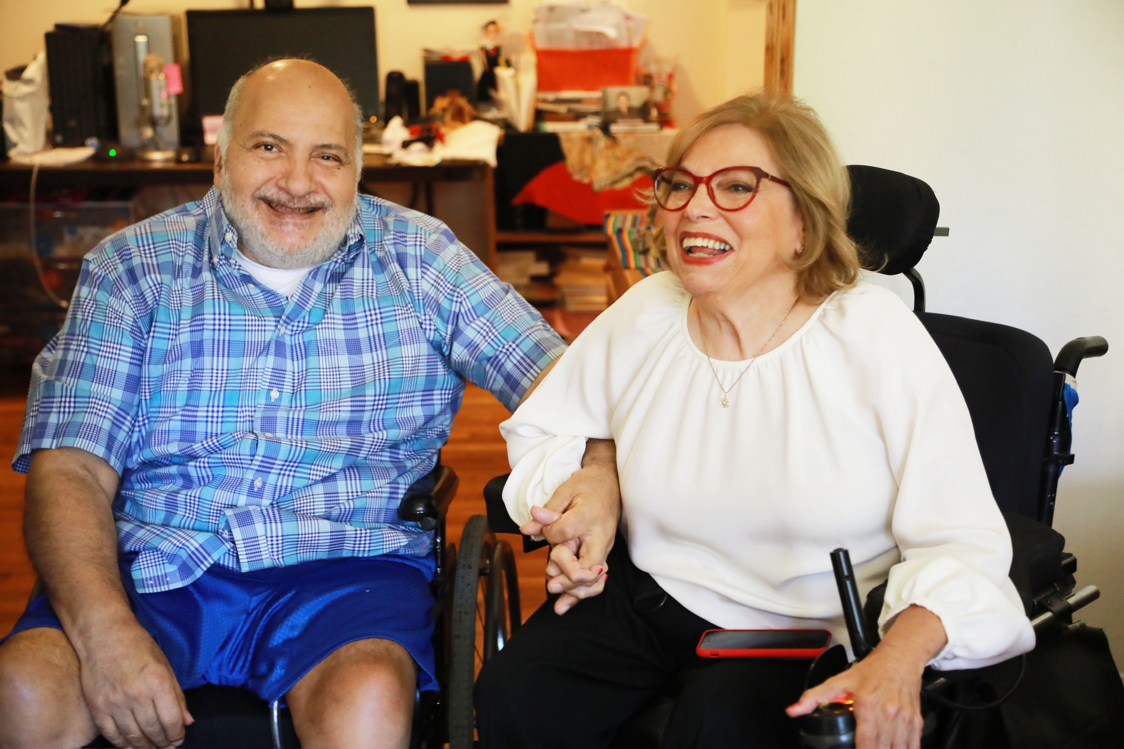 Judy Heumann and Jorge Pineda smiling and holding hands in their apartment